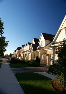 Row of suburban houses with well-maintained lawns and porches, under a clear blue sky during daytime