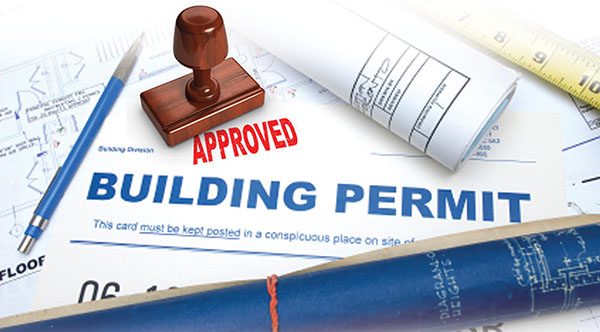 A contractor and homeowner discussing home remodeling permits with blueprints and permit documents in hand.